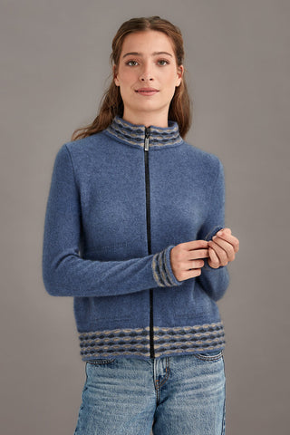 Woman wearing a blue zip-up sweater with patterned trim against a gray background