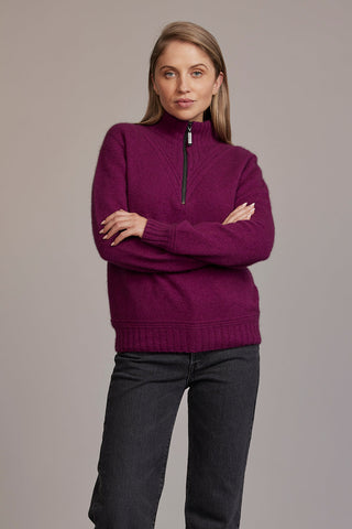 A woman wearing a berry McDonald sweater with a funnel neck and a 1/4 zip, paired with black pants.