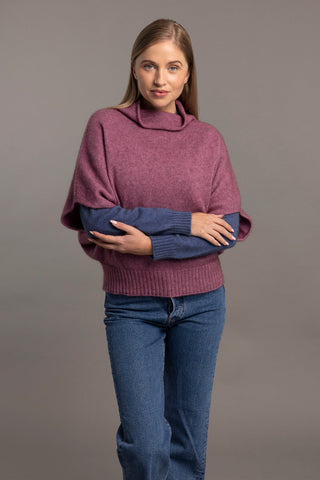 Woman wearing a heather pink shrug sweater over a blue long-sleeve shirt on a gray background