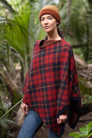 Woman wearing a spice and honeycomb knitted hat and tartan poncho sweater outdoors