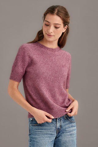 Woman wearing a heather pink t-shirt sweater and blue jeans against a gray background