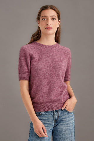 Woman wearing a heather pink t-shirt sweater and blue jeans against a gray background
