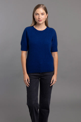 A woman wearing a cobalt blue t-shirt sweater with a stepped stitch design at the cuffs and hem, paired with black trousers.