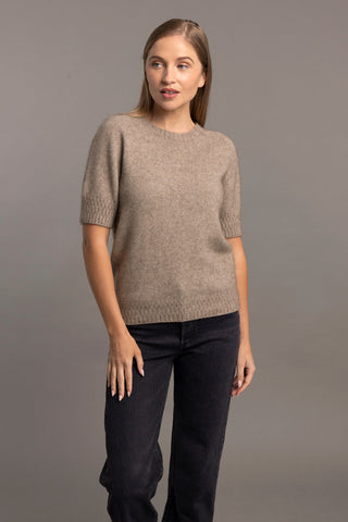 A woman wearing a mocha brown t-shirt sweater with a stepped stitch design at the cuffs and hem, paired with black trousers.