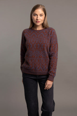 A woman wearing a red and blue toned Fair Isle pullover sweater with intricate patterns, paired with black pants.