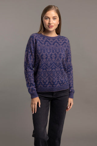A woman wearing a blue Fair Isle pullover sweater with intricate patterns, paired with black pants.