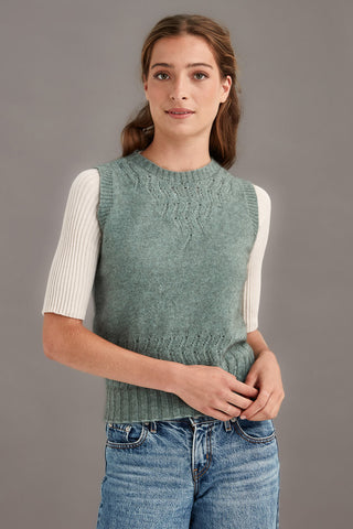 Woman wearing a mint green knitted vest over a white shirt with a gray background