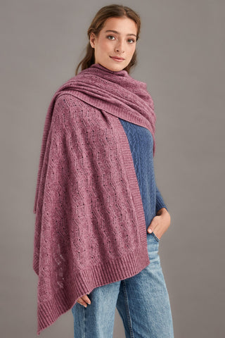 Woman wearing a heather pink knitted shawl over a blue sweater against a gray background