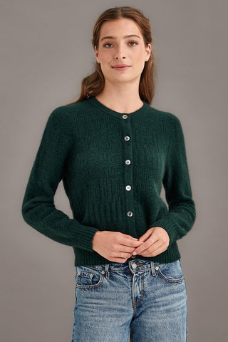 Woman wearing a green knitted cardigan and blue jeans against a gray background