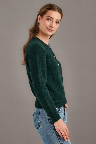 Woman wearing a green knitted cardigan and blue jeans against a gray background