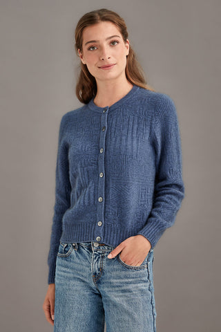 Woman wearing a blue knitted cardigan and jeans against a gray background