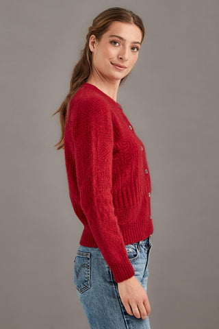 Woman wearing a red knitted sweater and blue jeans against a gray background