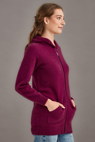 Woman wearing a berry pink hooded knit jacket against a gray background