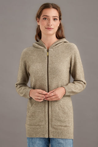 Woman wearing a beige brown hooded knit jacket against a gray background