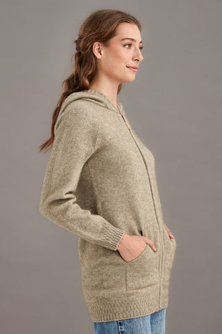 Woman wearing a beige brown hooded knit jacket against a gray background