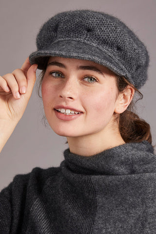 A woman wearing a gray soft peak hat, which is made of a mix of possum merino and mulberry silk fabrics.