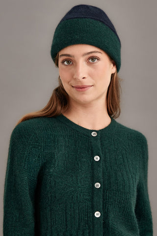 Woman wearing a dark green and navy knitted hat and cardigan against a gray background