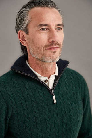 Man wearing a green cable knit sweater with a white shirt underneath against a gray background