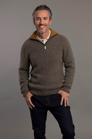 A man wearing a beige cable knit jersey with contrast trim against a grey background.