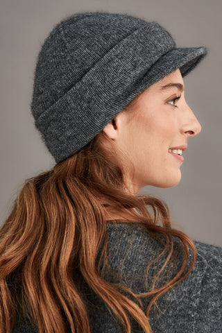 Woman wearing a gray knit cap with a visor against a neutral background