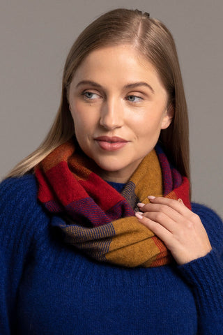A woman wearing a blue sweater and the Ombre Snood in a red and orange check pattern.