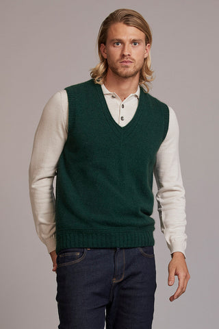 Man wearing a green sweater vest over a white shirt with a plain background