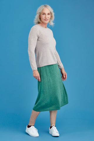 Woman wearing a light sand merino sweater and green skirt on a blue background