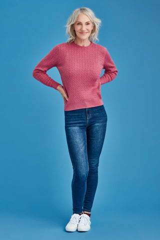 Woman wearing a pink merino sweater and blue jeans against a blue background