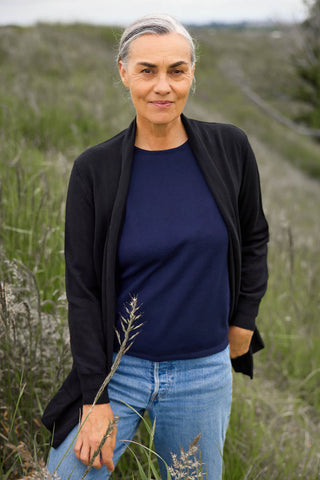 A woman standing in a field wearing a black long cardigan with an open front design, paired with blue jeans.