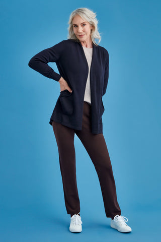 Woman wearing a navy long merino cardigan, white shirt, brown pants, and white sneakers on a blue background