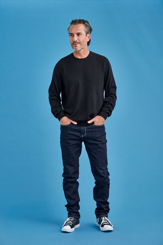 Man wearing a black sweater and jeans standing against a blue background