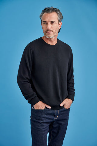 Man wearing a black sweater and blue jeans against a blue background