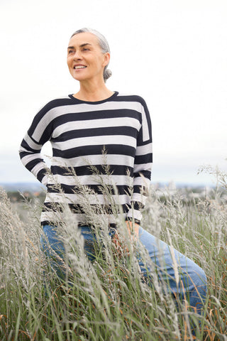 A woman standing outdoors wearing a grey and white striped drop shoulder jumper