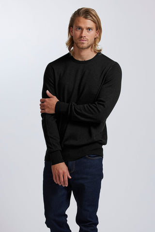 Man wearing a black sweater and jeans standing against a white background