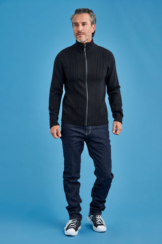 Man wearing a black zip-up sweater and dark jeans against a blue background