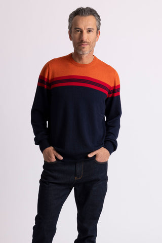 A man wearing a orange and dark navy variegated crew neck sweater and blue jeans.