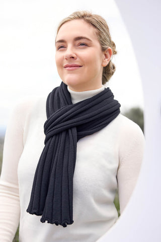 A woman wearing a black rib scarf wrapped around her neck, paired with a white top.