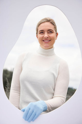 A person standing outside with a white frame wearing a ribbed merino glove, smiling.