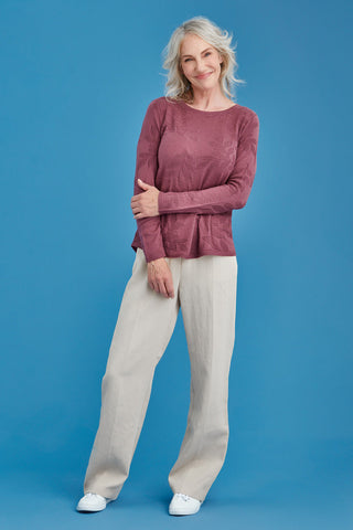 Woman wearing a mauve sweater and beige pants against a blue background