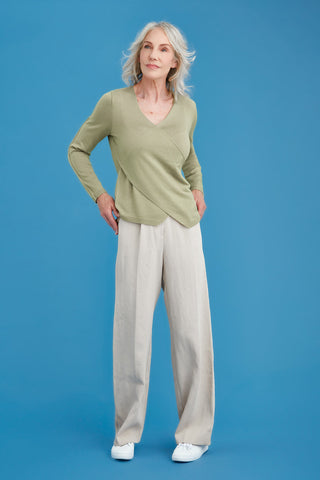 Woman wearing a green merino sweater and beige pants on a blue background