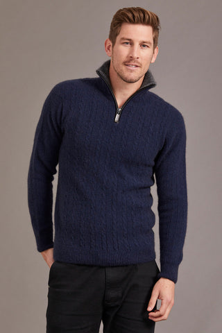 A man wearing a blue cable knit jersey with contrast trim against a grey background.