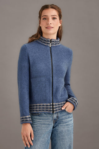 Woman wearing a blue zip-up jacket with a wave detailing against a gray background