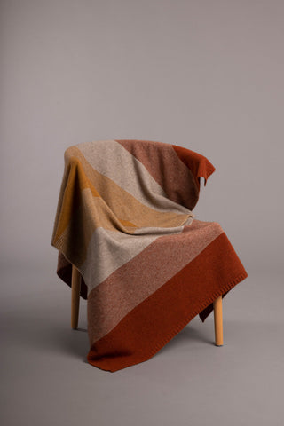 A harvest multicolored ombre pattern throw draped over a chair.