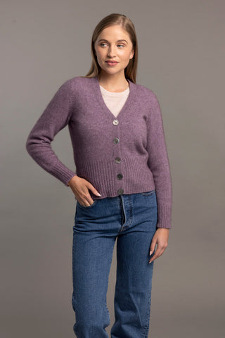 Woman wearing a lilac purple cardigan over a white shirt with blue jeans on a gray background