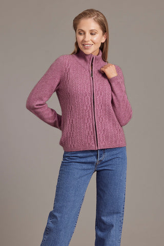 A woman wearing a heather pink zip-up jacket with lace cable detailing, paired with blue jeans.