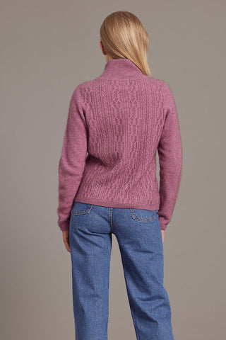 A woman wearing a heather pink zip-up jacket with lace cable detailing, paired with blue jeans.