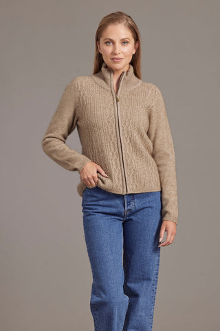 A woman wearing a beige zip-up jacket with lace cable detailing, paired with blue jeans.