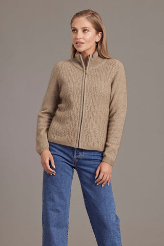 A woman wearing a beige zip-up jacket with lace cable detailing, paired with blue jeans.