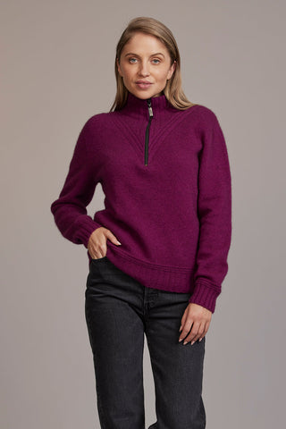 A woman wearing a berry McDonald sweater with a funnel neck and a 1/4 zip, paired with black pants.