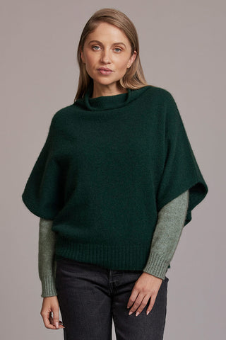 Woman wearing a dark green shrug sweater over a matching long-sleeve shirt on a gray background